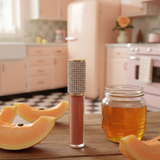 Lip gloss with decorative cap on a table with honey and melon slices, kitchen in the background