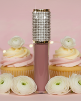 Lip gloss with decorative crystals surrounded by cupcakes and yellow flowers on a pink background