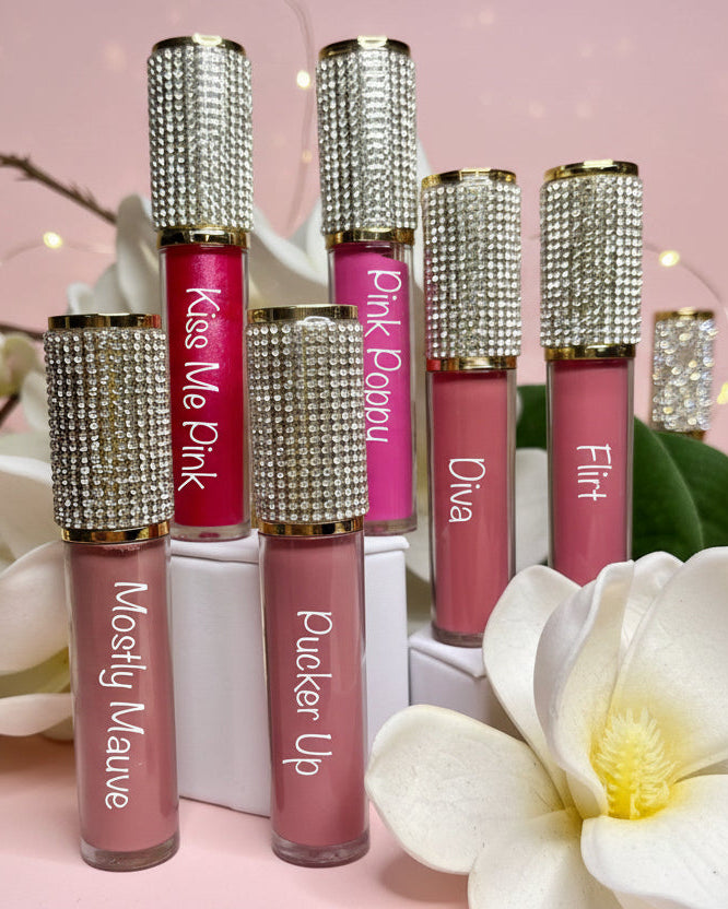 Set of matte lipsticks with rhinestone caps on a pink background with flowers.