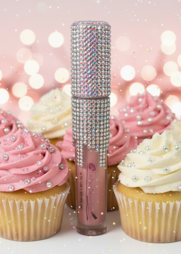 Lip gloss with rhinestone top surrounded by cupcakes on a light background with lights