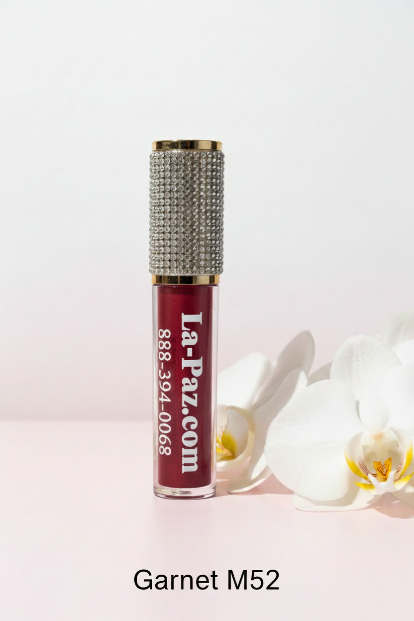 La Paz Cosmetics M52 Garnet Diamond Liquid Matte Lipstick tube with rhinestone cap on a soft blush background, showing the deep brownish-red shimmering formula through the clear tube