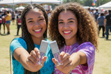 Two young women holding up small lip oil bottles at a festival