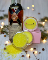 La Paz Cosmetics Vanilla Lip Sugar Scrub and Mask — open scrub jar with yellow sugar crystals spilling out and lip mask jar beside a vintage vanilla extract bottle and pink La Paz gift box on a white wood surface with warm bokeh fairy lights