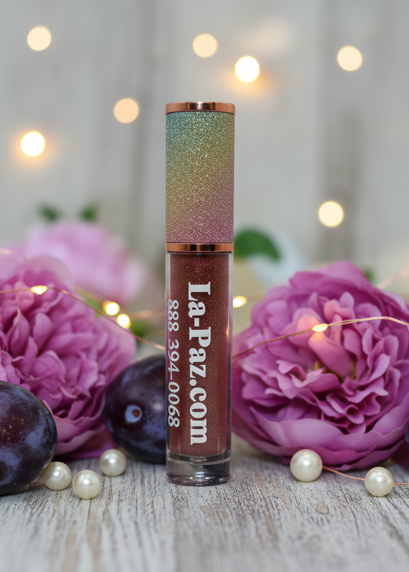 Lip gloss with glittery cap and visible brand name against a blurred floral background