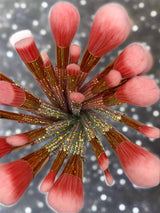 La Paz Cosmetics Pink Bling Makeup Brush Collection — overhead view of all brushes fanned out with pink bristles and iridescent crystal-covered handles on a silver glitter background