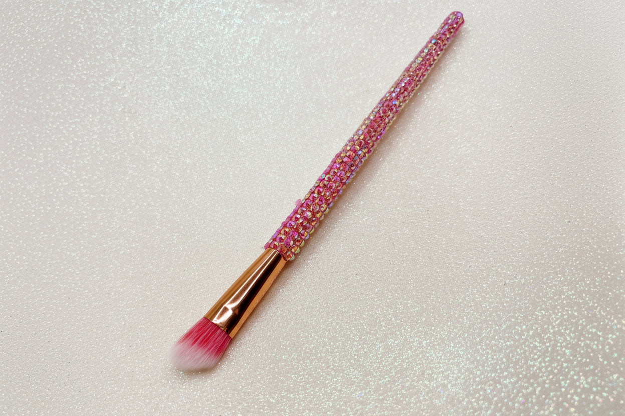 Angled eye makeup brush with pink bristles and a pink rhinestone handle on a sparkly background by La Paz Cosmetics