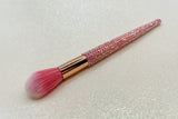 Round blush brush with pink bristles and a pink rhinestone handle on a sparkly background by La Paz Cosmetics