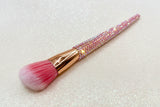 Angled blusher brush with pink bristles and a pink rhinestone handle on a sparkly background by La Paz Cosmetics
