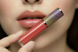 Close-up of a hand holding a pink lip gloss with a glittery cap.