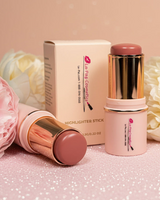 La Paz Cosmetics Cream Blush Stick in Buttercup 04 — two gold and cream sticks open and closed beside the La Paz Cosmetics box, surrounded by white and blush peony flowers on a warm beige background