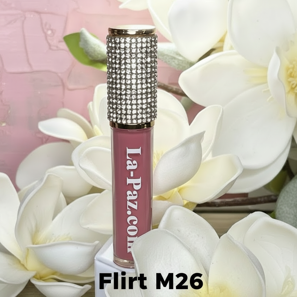 La Paz Cosmetics M26 Flirt Diamond Liquid Matte Lipstick tube with rhinestone cap nestled among white magnolia flowers on a soft pink background