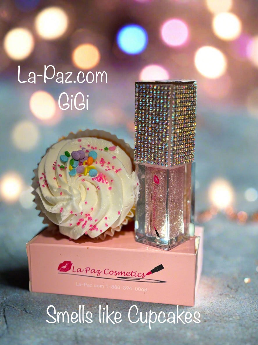 GiGi Glittr Lip Oil  with a cupcake and 'La Paz Cosmetics' packaging on a blurred lights background.