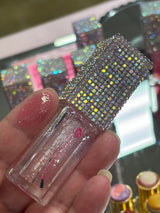 Hand holding a tube of GiGi Glitter Lip Oil with a swatch of the clear glitter oil on a finger tip.