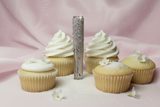 frosted lip gloss with rhinestones next to a cupcake on a pink fabric background