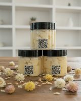 Three jars helichrysum cream on a wooden surface with flowers, in a kitchen setting.