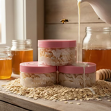 Jars of honey and containers of oatmeal milk and honey body butter on a wooden surface with a bee flying over.