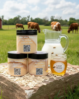 Three jars of 'Miss Moo Belle' Oatmeal Milk & Honey by La Paz in a field with cows and a red barn.