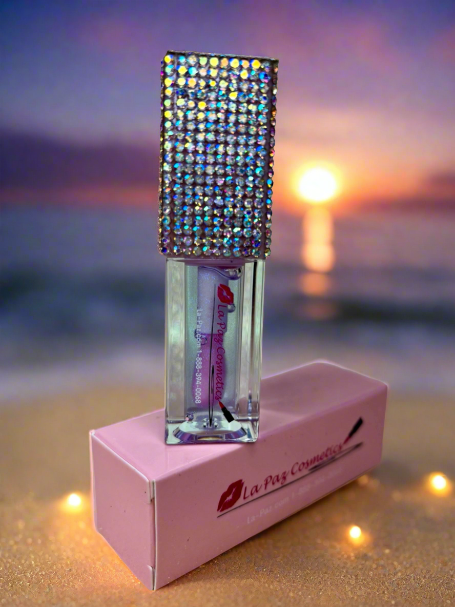 Oceans lip oil with rhinestone top on a pink box against a sunset beach background