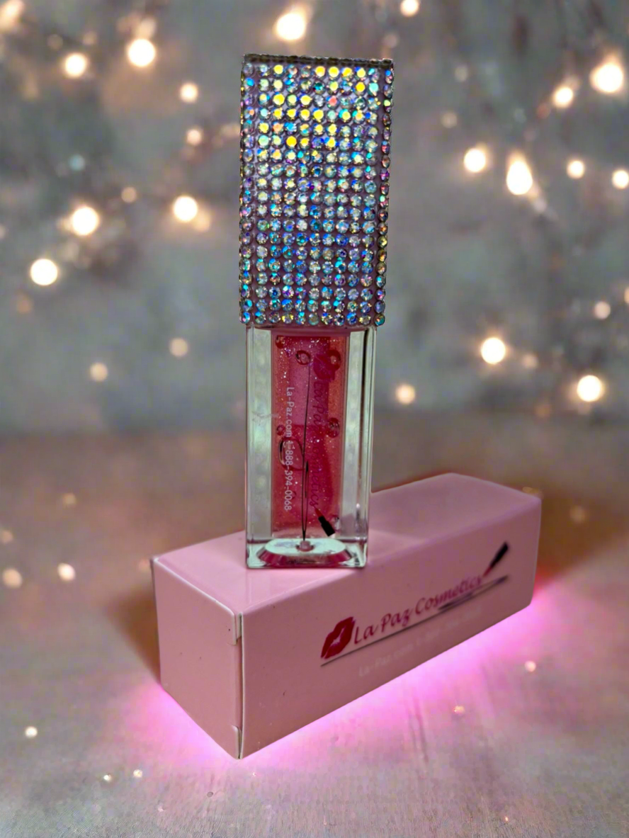 Lip oil in Pink Me with rhinestone top on a pink stand against a blurred light background