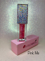 A bottle of Pink Me Glowing Lip Oil with a multicolored crystal-encrusted cap, displayed alongside its pink box.