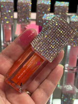 Hand holding Venus lip oil with a rhinestone top and a swatch on a fingertip