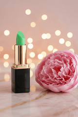 A tube of L'Paige brand green color changing lipstick styled with a pink peony blossom presented by La Paz Cosmetics