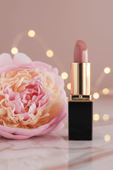 A tube of L'Paige lipstick in shade #38 Champagne with a gold cap, displayed against a mauve with bokeh fairy lights in background.