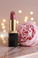 L'Paige Lipstick in color #45 Icy Mauve with a black tube, gold collar, and is  standing beside a large pink flower