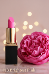 #18 Brightest Pink L'Paige Lipstick shade with a gold and black container. Presented by La Paz  Cosmetics and styled with a pink peony and bokeh lights in background
