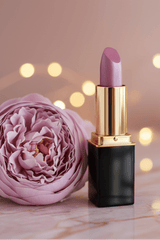 A lipstick tube of #53 Amethyst Mist with a black and gold tube standing beside a large pink flower