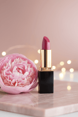 #20 L'Paige Lipstick in a gold and black tube with bokeh lights in the background and a peony blossom