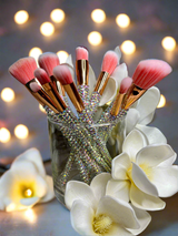 La Paz Cosmetics - Aurora Bling makeup brushes in a decorative holder with flowers and blurred lights in the background
