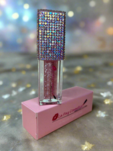 GiGi Glitter lip oil with rhinestone top on pink stand against a glittery background