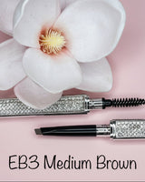 La Paz Cosmetics Luxe Crystal Eyebrow Pencil EB3 Medium Brown open showing dual-ended design with spoolie and precision tip, crystal case on pink background with white orchid