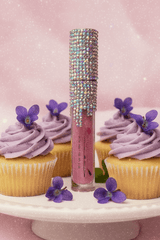 La Paz Crystal Frosting Lip Gloss Sugared Violets D20 — crystal tube, purple cupcakes & violet flowers on pink background