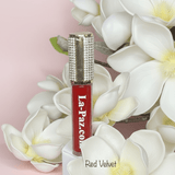 La Paz M40 Red Velvet Diamond Liquid Matte Lipstick with rhinestone cap among white magnolia flowers on pink background