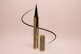 La Paz Cosmetics Luxe Felt Tip Liquid Eyeliner in Black — rhinestone and gold pen open with ultra-fine felt tip displayed beside a dramatic black swoosh line on a blush pink background