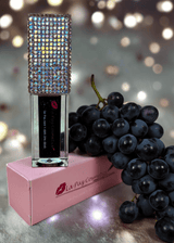 Black Magic color changing lip oil styled with grapes and bokeh lights in background