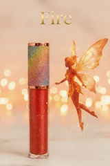 La Paz Fire Lux Lip Gloss with golden fire fairy figurine on light surface against warm glowing bokeh background