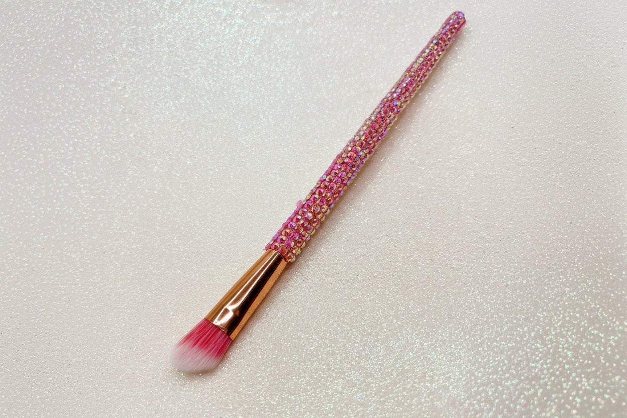 Angled eye makeup brush with pink bristles and a pink rhinestone handle on a sparkly background by La Paz Cosmetics