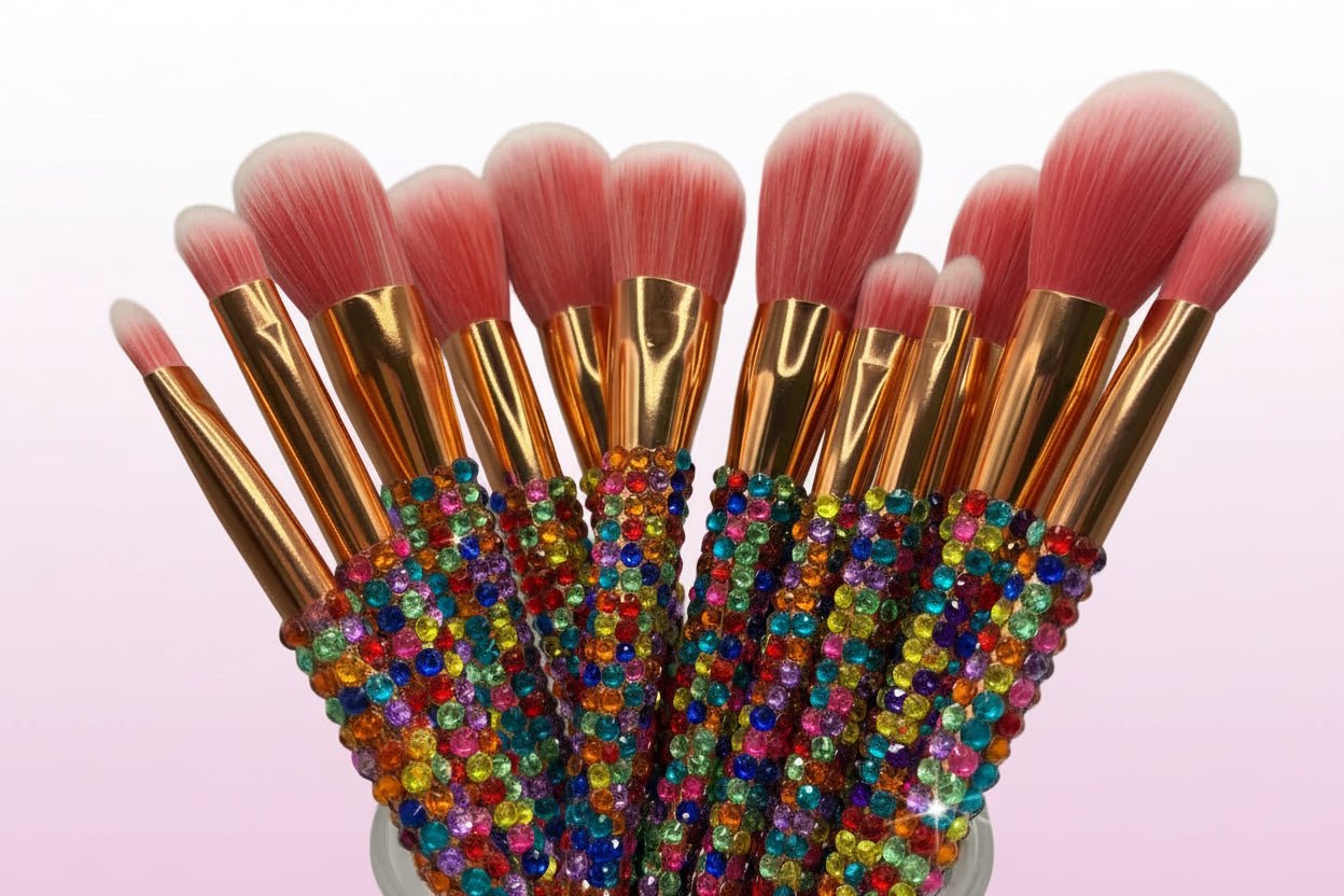 Makeup brushes with gold ferrules and pink bristles, some covered in multicolored crystals