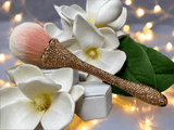 Bling Bling Powder Brush with rose gold rhinestones by La Paz Cosmetics. Displayed with white flowers with blurred lights in the background