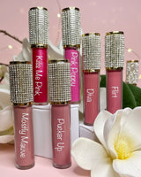 Set of lip glosses with rhinestone caps on a pink background with flowers.